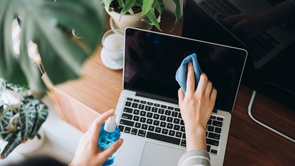 person cleaning the surface of laptop with cleaning spray and cloth