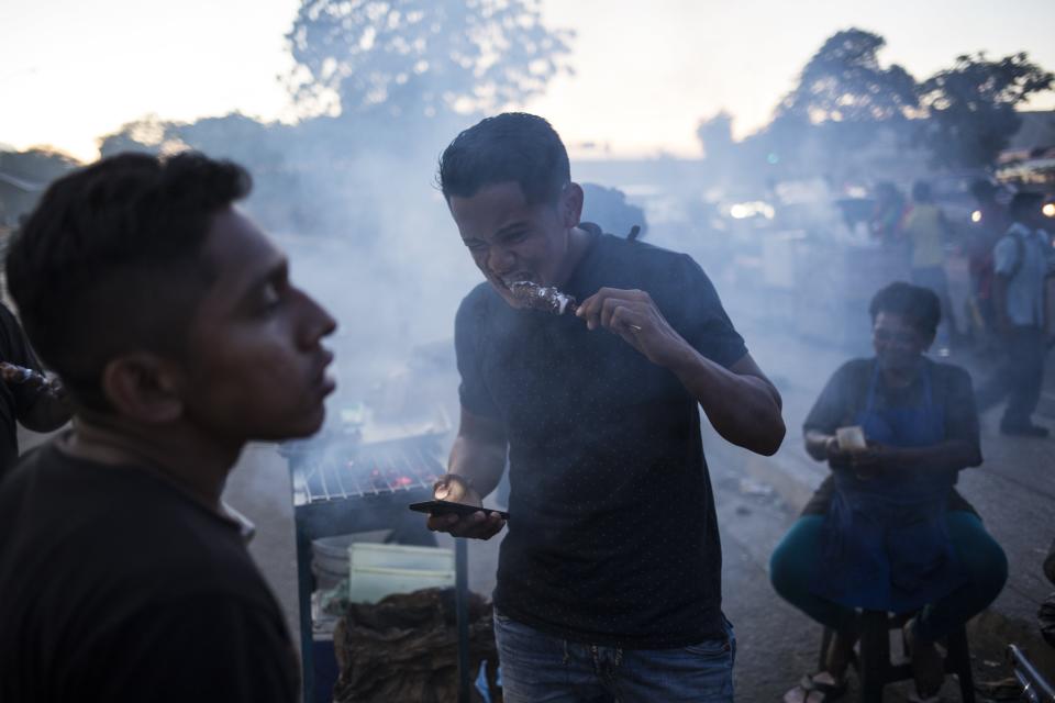 In this Nov. 15, 2019 photo, a man eats a kebab in "Las Pulgas" market in Maracaibo, Venezuela. Nationwide, an estimated 4.5 million residents have fled Venezuela, most going to nearby Colombia, Peru and Ecuador. They search for better jobs to send money home, but they often confront backlash and hardships as their numbers steadily grow. (AP Photo/Rodrigo Abd)