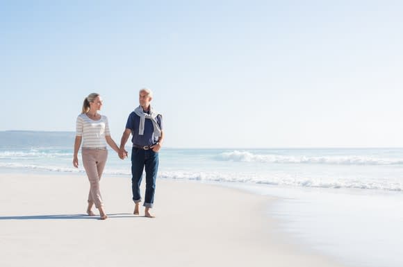 An older couple takes a walk on the beach.