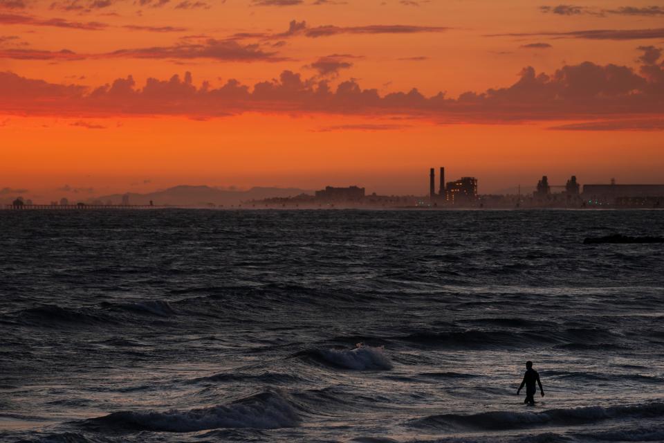A man wades into the ocean at sunset on June 22, 2021, in Newport Beach, Calif. The National Oceanic and Atmospheric Administration announced Friday that the amount of carbon dioxide in the atmosphere in May averaged 421 parts per million, more than 50% higher than pre-industrial levels.