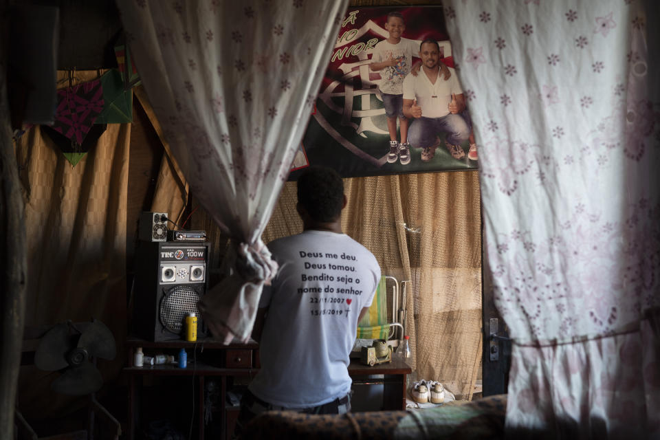 In this June 20, 2019 photo Jocely Rozario Junior, the father of Kaua, who was killed by a stray bullet, stands in front of a souvenir poster showing his son and himself, in home at the Vila Alianca slum in Rio de Janeiro, Brazil. "The governor's men are going out to shoot at innocent people," said Rozário Junior, who blames the May 16th death of his 11-year-old son on police gunfire. (AP Photo/Leo Correa)