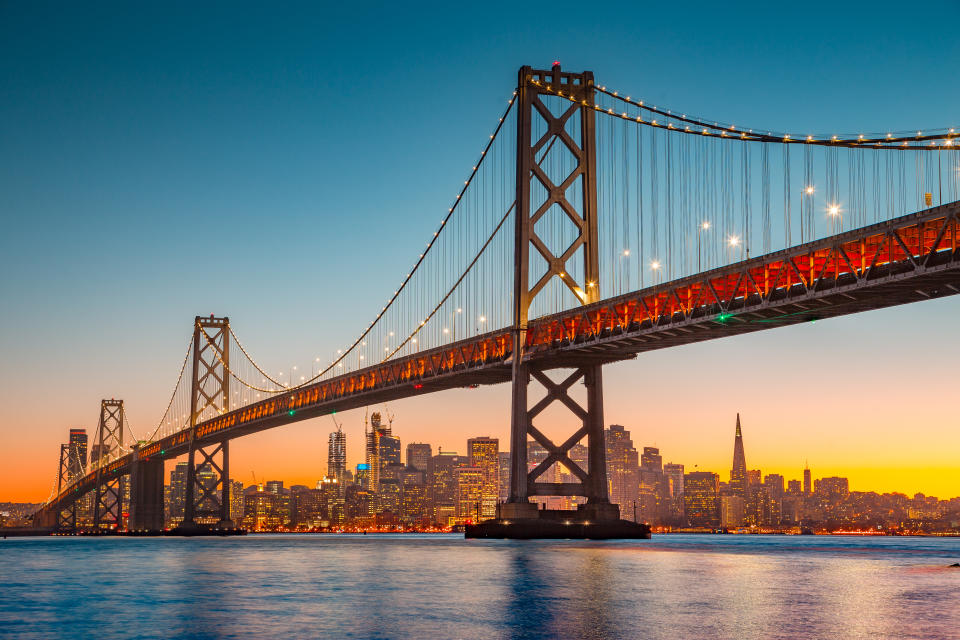 Classic panoramic view of San Francisco skyline with famous Oakland Bay Bridge illuminated in beautiful golden evening light at sunset in summer, San Francisco Bay Area, California, USA