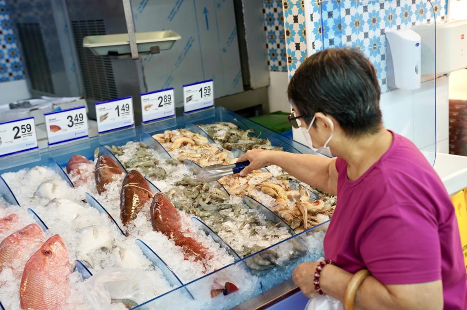 Customer picking fresh gray shrimp in Pasar. It explains that FairPrice Group froze prices during the RMB period.