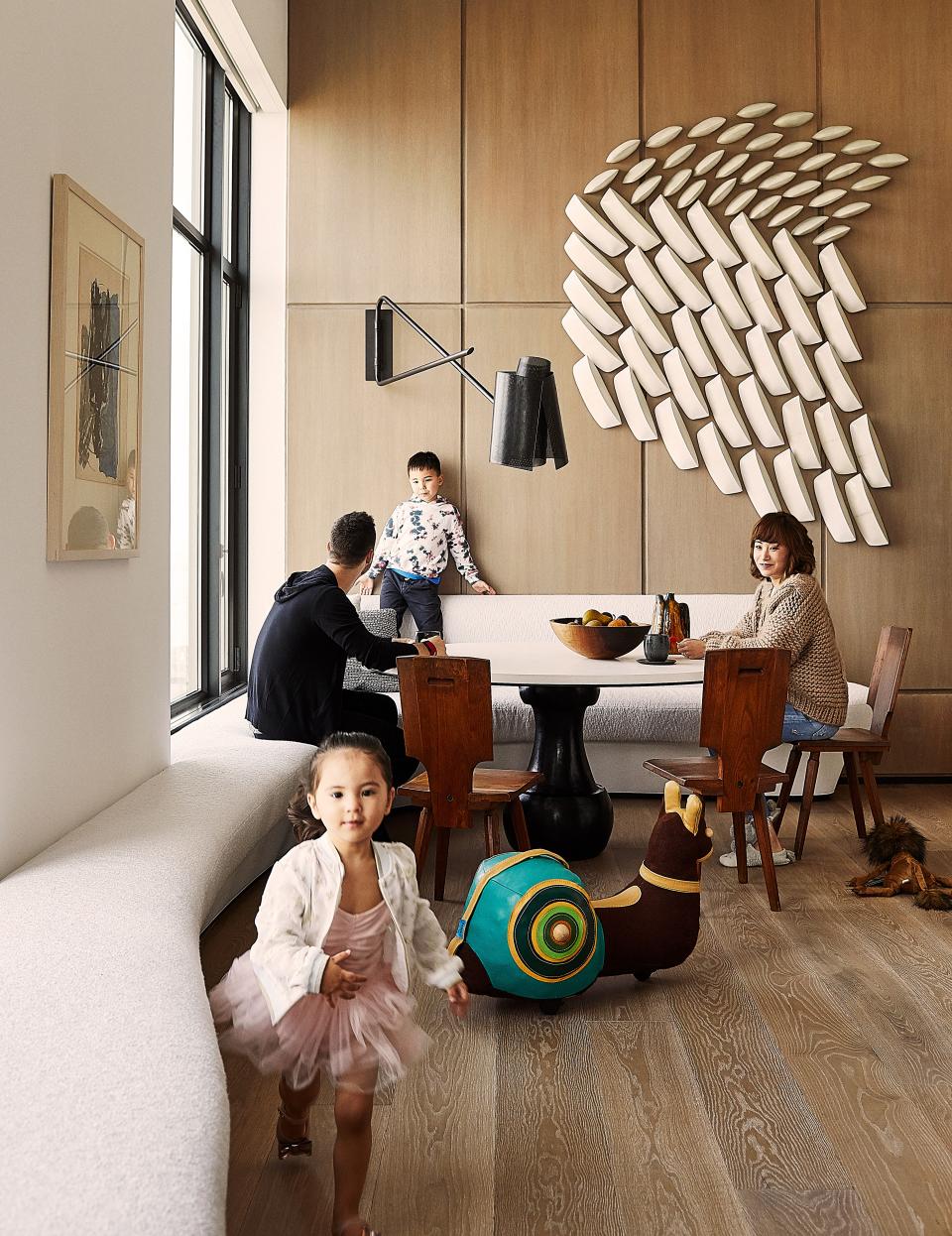 The family sits at a table by Michel Amar; vintage chairs by Pierre Chapo. Custom Banquette in a Holly Hunt performance fabric; Pierre Yovanovitch wall lamp; Artwork by Maren Kloppmann.