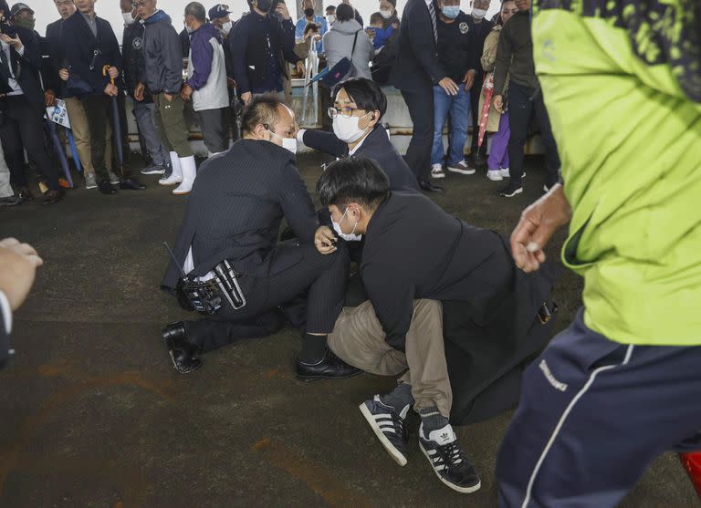 Policías someten contra el piso a un hombre que al parecer lanzó una bomba de humo durante la visita del primer ministro Fumio Kishida a un puerto en la prefectura de Wakayama, oeste de Japón, el sábado 15 de abril de 2023.