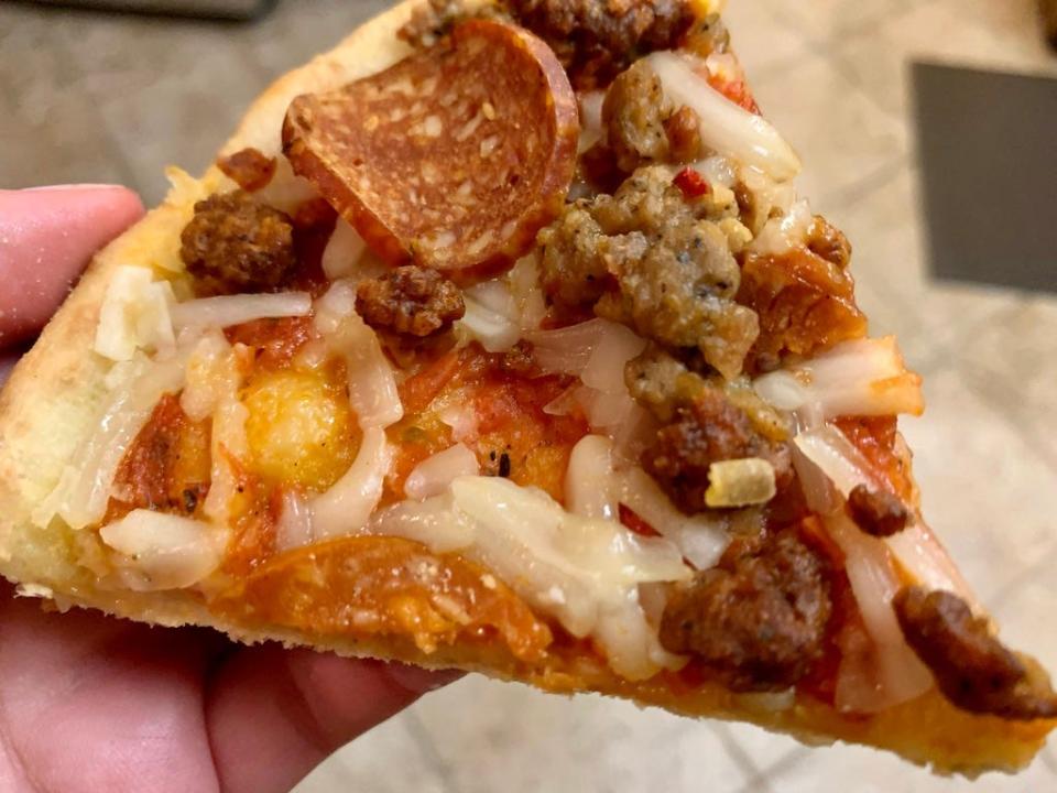 Hand holding slice of trader joe's meat-lover vegan pizza