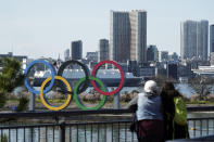 In this Tuesday, March 3, 2020, photo, tourists look at the Olympic rings, at Tokyo's Odaiba district in Tokyo. Japan's Olympic minister has suggested in Parliament that the Tokyo Olympics might be pushed back a few months from it July 24 opening. The games are under threat from a spreading virus from China that has reached the pandemic stage. But the so-called “Home City Contract”signed by the International Olympic Committee and Japanese officials gives the IOC wide latitude in terminating the Olympics. (AP Photo/Eugene Hoshiko)