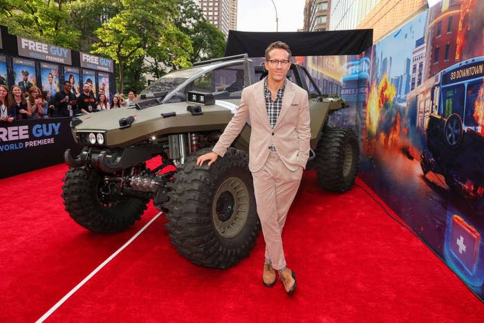 Ryan Reynolds attends the World Premiere of 20th Century Studios' Free Guy and stands in front of a large vehicle