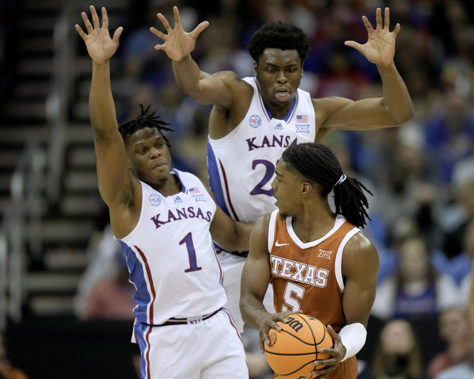 Texas guard Marcus Carr (5) looks to pass around Kansas guard Joseph Yesufu (1) and center Ernest Udeh Jr. during the second half of the NCAA college basketball championship game of the Big 12 Conference tournament Saturday, March 11, 2023, in Kansas City, Mo. (AP Photo/Charlie Riedel)