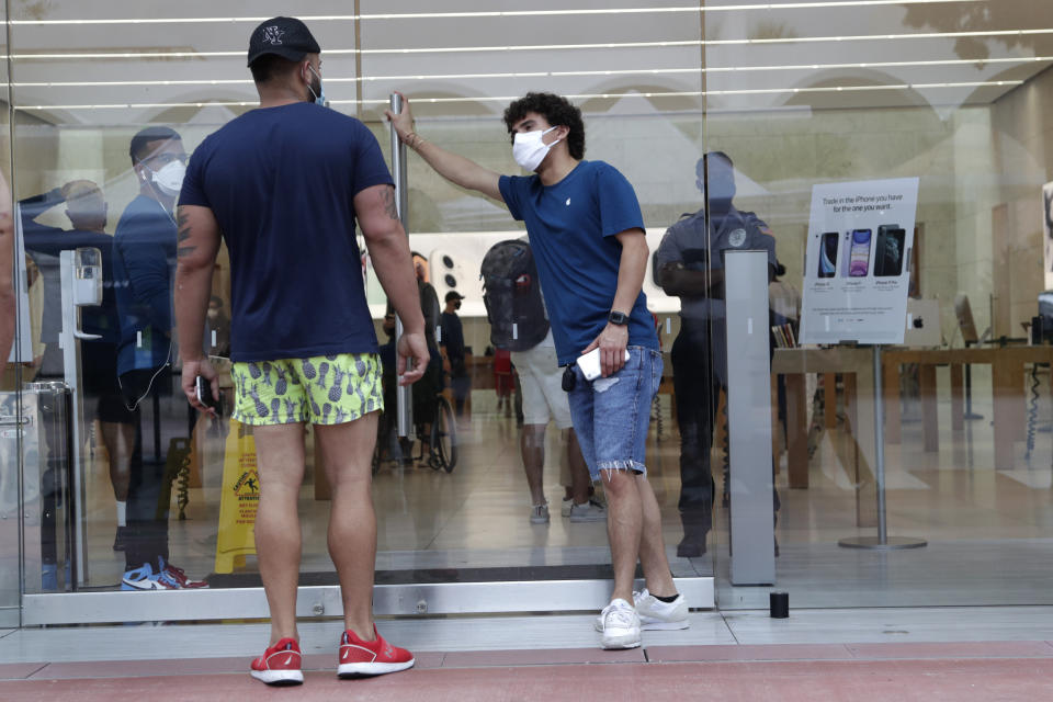 An employee wearing a protective face covering, right, monitors the flow of customers at an Apple retail store along Lincoln Road Mall during the new coronavirus pandemic, Wednesday, June 17, 2020, in Miami Beach, Fla. (AP Photo/Lynne Sladky)