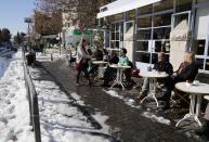 Customers sit at a cafe on a snow-covered street in Jerusalem December 15, 2013. Jerusalem's heaviest snow for 50 years forced Israeli authorities to lift a Jewish Sabbath public transport ban on Saturday and allow trains out of the city where highways were shut to traffic. REUTERS/Darren Whiteside (JERUSALEM - Tags: ENVIRONMENT SOCIETY)