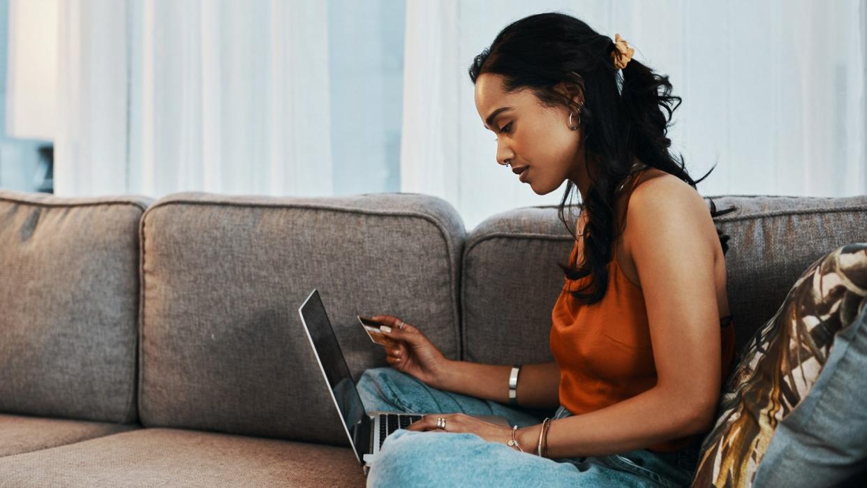 Shot of a young woman using a laptop and credit card on the sofa at home.