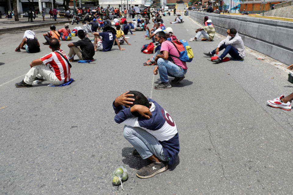 Pictured is a man squatting and covering his head in the middle of a street in Venezuela as others around him are also forced to sit in the street for breaking coronavirus rules. 