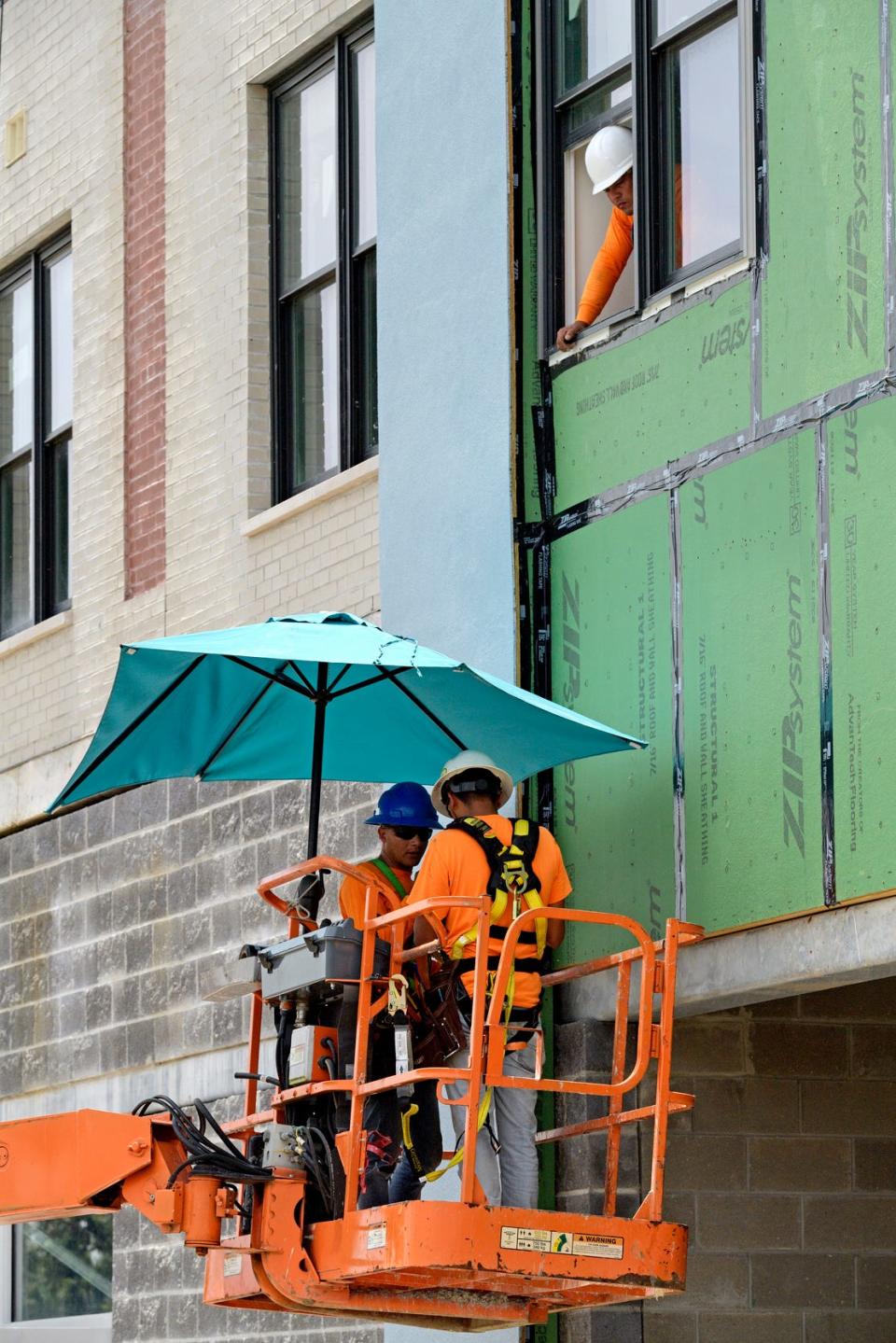 Construction workers keep out of the sun with an umbrella on their boom lift as they work on an apartment building along South Jefferson Davis Parkway in New Orleans on Aug. 13.