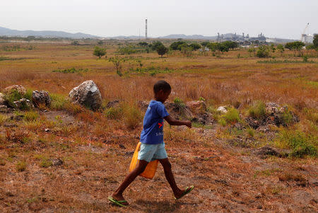 The ExxonMobil PNG Limited operated Liquefied Natural Gas (LNG) plant can be seen behind a boy as he carries a container to collect water in the village of Papa Lea Lea located at Caution Bay on the outskirts of Port Moresby, Papua New Guinea, November 19, 2018. Picture taken November 19, 2018. REUTERS/David Gray