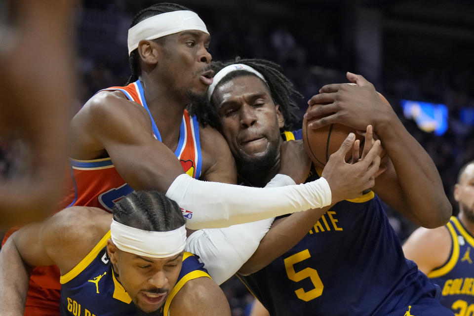 Oklahoma City Thunder guard Shai Gilgeous-Alexander, top left, reaches for the ball against Golden State Warriors forward Kevon Looney (5) and guard Moses Moody, bottom, during the first half of an NBA basketball game in San Francisco, Tuesday, April 4, 2023. (AP Photo/Jeff Chiu)