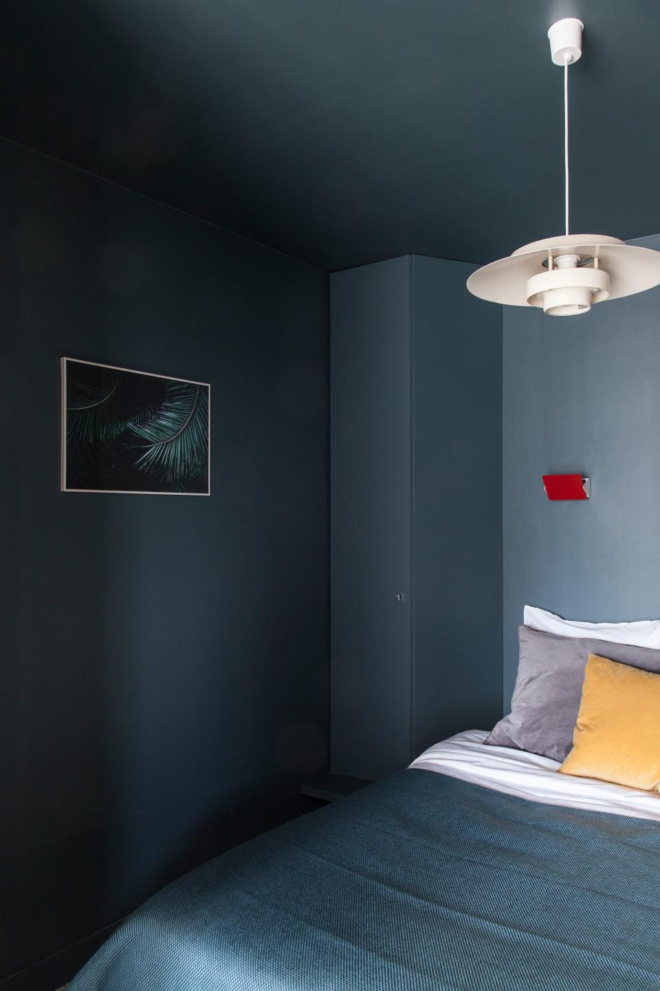 A dark paint was selected because the bedroom was going to be dark no matter what, resulting in a cocoon-like vibe. Cheerful accents abound—peep those red Perriand sconces.