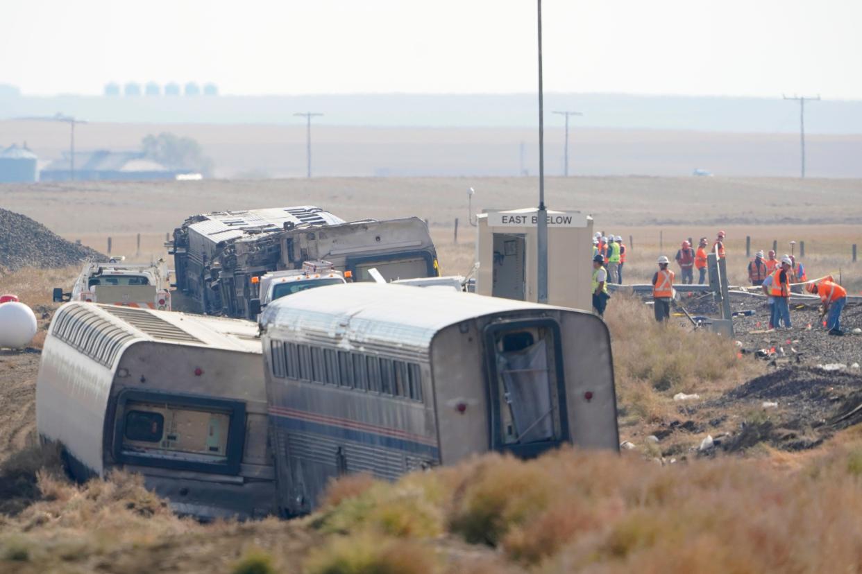 In this Sept. 27, 2021, file photo, workers stand near train tracks next to overturned cars from an Amtrak train that derailed near Joplin, Mont. A derailment of an Amtrak train in Montana that killed three people in 2021 was caused by a railroad track that was bent along a curve near the accident site, federal investigators said Thursday, July 27, 2023 in a final report. (AP Photo/Ted S. Warren, File)