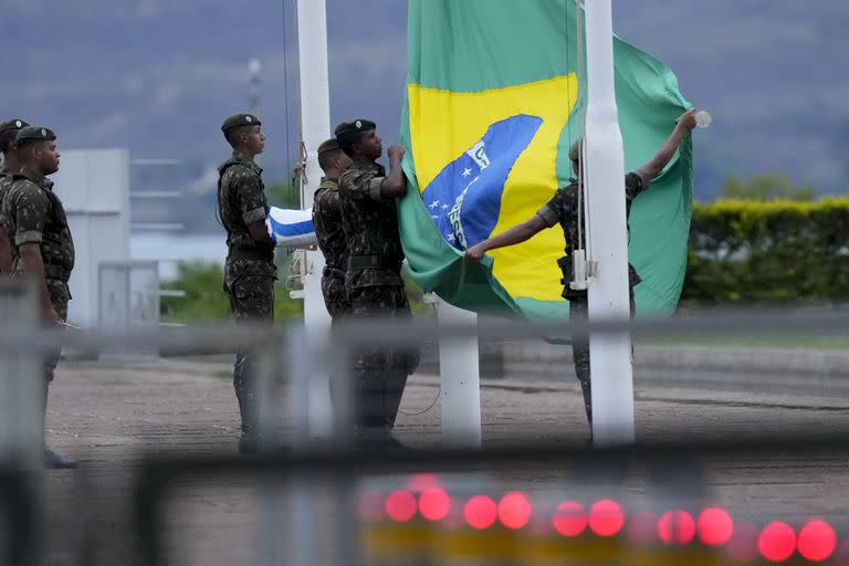 Soldados bajan la bandera brasileña durante una ceremonia frente al Palacio Alvorada, la residencia oficial de los brasileños, después del cierre de las urnas para las elecciones generales en Brasilia, Brasil, el domingo 2 de octubre de 2022. (Foto AP/Eraldo Peres)
