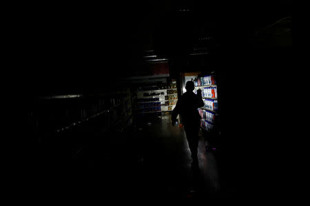 A worker inspects damage in a supermarket after it was looted during an ongoing blackout in Caracas, Venezuela March 10, 2019. REUTERS/Carlos Garcia Rawlins