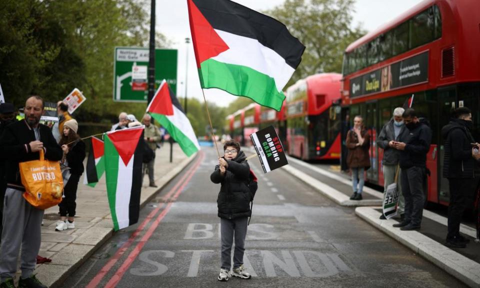 A boy waves a Palestinian flag  next to red London buses