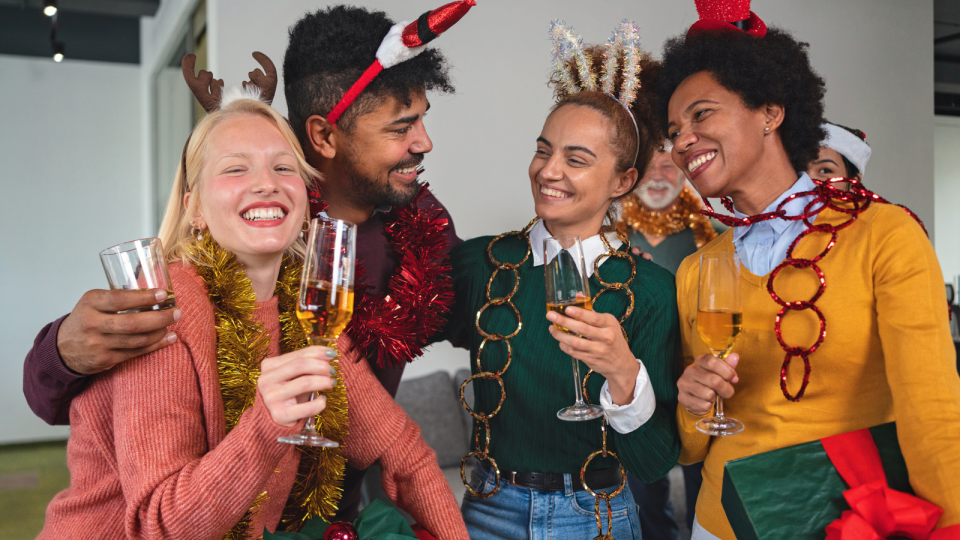 A group of colleagues drink champagne while dressed in a Christmas theme for a work party.