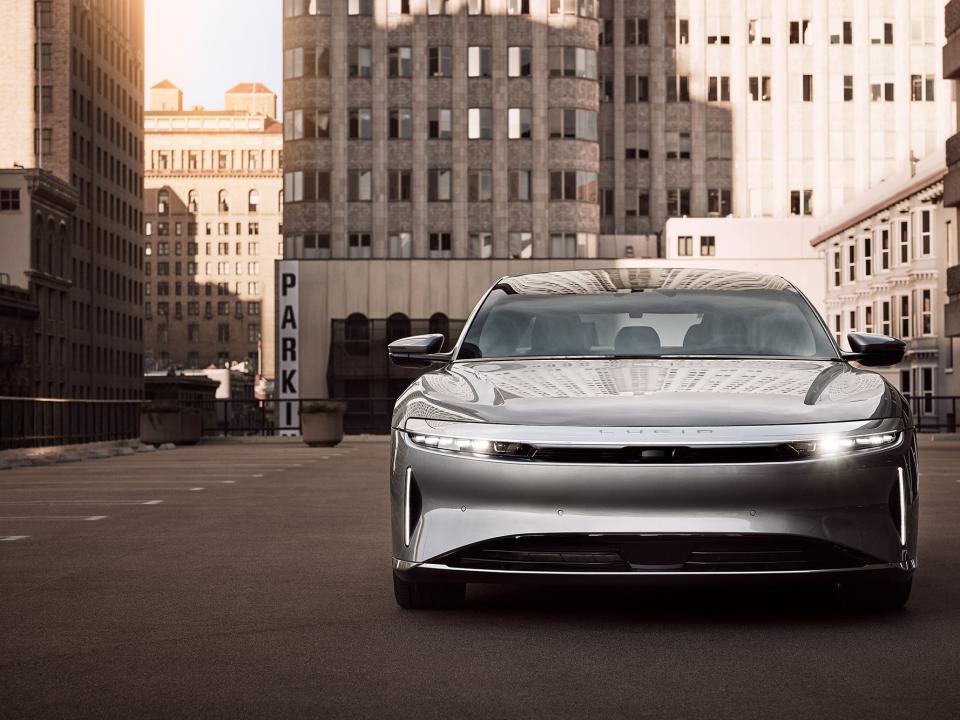 A sleek, silver sedan parked on the road in front of several city buildings.