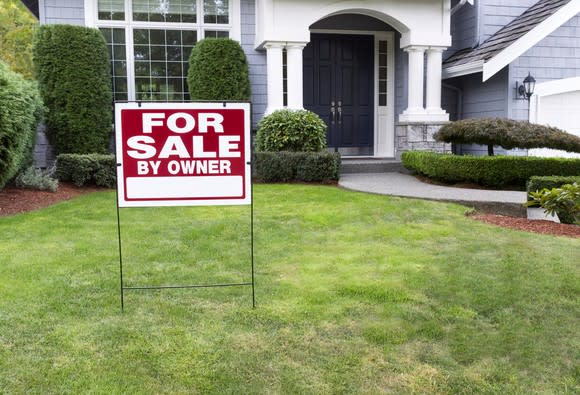 A for sale by owner sign is on the lawn in front of a house.