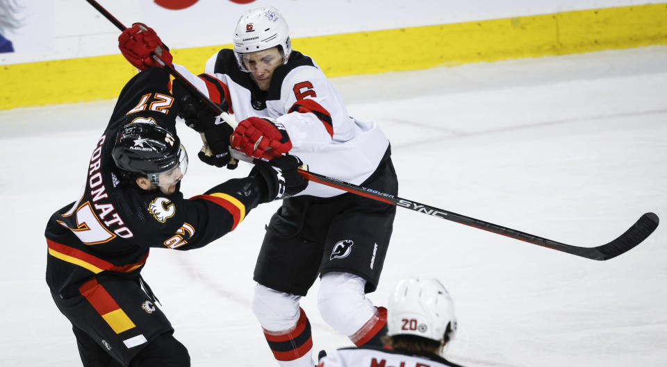 New Jersey Devils defenseman John Marino, right, checks Calgary Flames forward Matthew Coronato during the second period of an NHL hockey match in Calgary, Alberta, Saturday, Dec. 9, 2023. (Jeff McIntosh/The Canadian Press via AP)