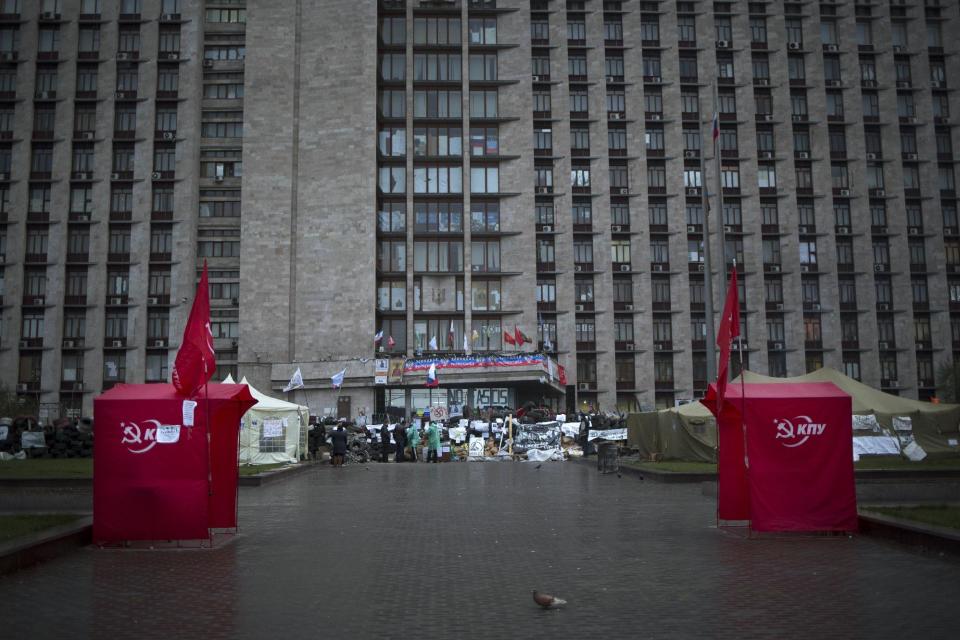 People stand near a tent camp and barricades set up in front of a regional administration building that was seized by pro-Russian activists earlier in Donetsk, Ukraine, early Sunday, April 20, 2014. Pro-Russian insurgents defiantly refused Friday to surrender their weapons or give up government buildings in eastern Ukraine, despite a diplomatic accord reached in Geneva and overtures from the government in Kiev. (AP Photo/Alexander Zemlianichenko)