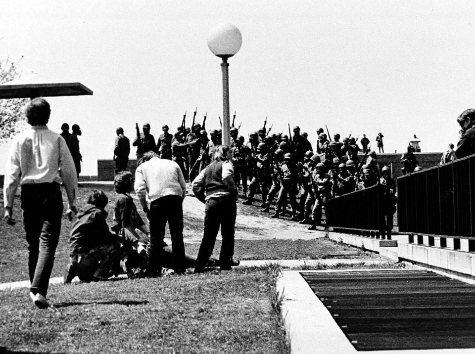 FIL - In this May 4, 1970 file photo, a group of youths cluster around a wounded person as Ohio National Guardsmen, wearing gas masks, hold their weapons in the background, on Kent State University campus in Kent, Ohio. Members of the Guard killed four students and injured nine during the campus protest against the Vietnam War. The school, about 30 miles southeast of downtown Cleveland, had planned an elaborate multi-day commemoration for the 50th anniversary Monday, May 4, 2020. The events were canceled because of social distancing restrictions amid the coronavirus pandemic. Some events, activities and resources are being made available online. (AP Photo/Douglas Moore, File)