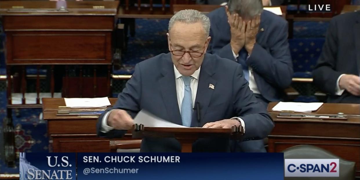 Sen. Chuck Schumer of New Yorker speaks following a cloture vote on a measure to raise the debt ceiling as Sen. Joe Manchin sits, visibly upset, behind him.