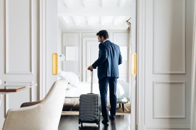 Businessman with wheeled luggage in suite