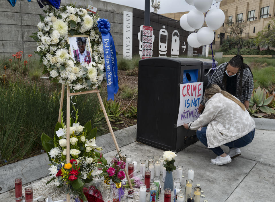 FILE - Nursing student Samantha Mesa hangs a sign in downtown Los Angeles on Jan. 19, 2022, with registered nurse Terri Thompson, right, in support of Sandra Shells at a memorial set up to her at the bus stop where she was attacked. Three random killings: a woman pushed in front of a train, another punched at a bus stop and a third stabbed to death while working alone in a store, and three homeless men charged with the crimes have reignited anger and frustration with the intractable issue of homelessness in New York and Los Angeles. (AP Photo/Richard Vogel, File)