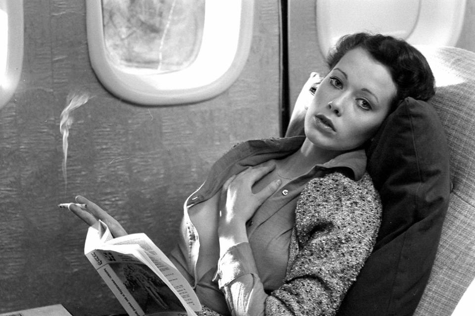 <p>Dutch actress Sylvia Kristel enjoys a cigarette and a book during a flight in 1974.</p>