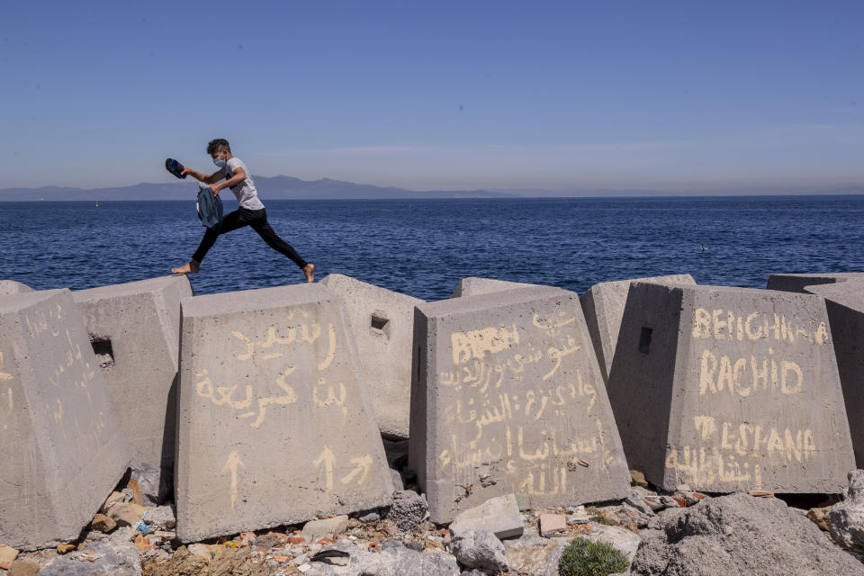 A migrant walks along the breakwater in the Spanish enclave of Ceuta, near the border of Morocco and Spain, Wednesday, May 19, 2021. Spain's north African enclave of Ceuta has awakened to a humanitarian crisis after thousands of migrants who crossed over from Morocco spent the night sleeping where they could find shelter. (AP Photo/Bernat Armangue)