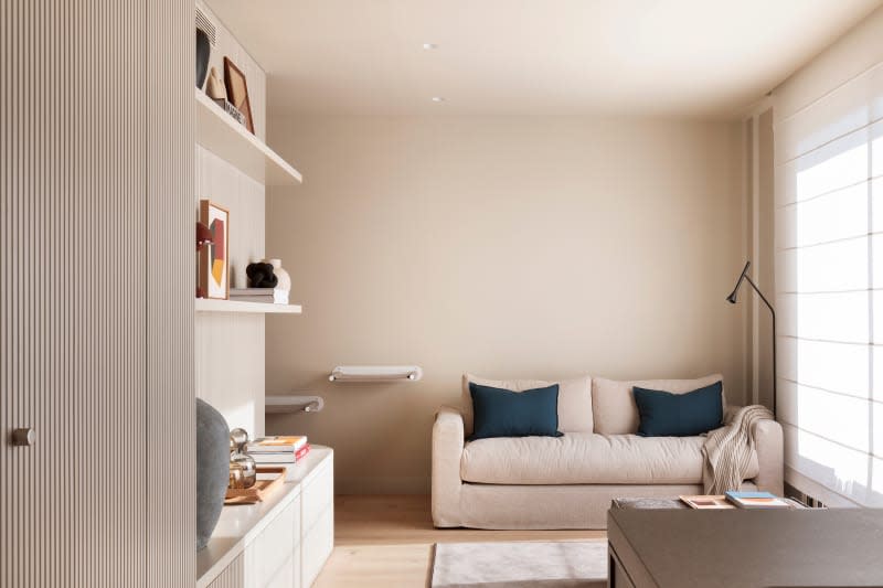 minimal beige living room with beige sofa , built in fluted shelves, and white sheer window shades