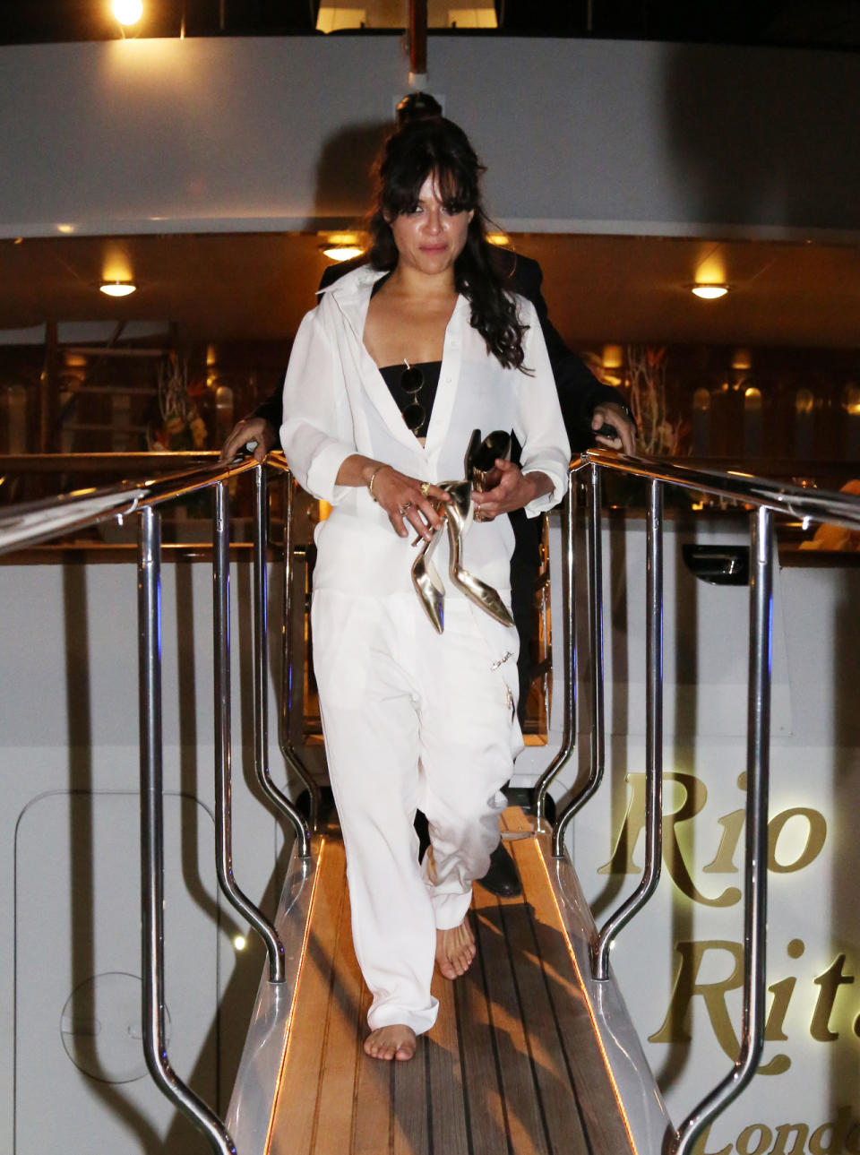 The Fast & Furious actress wears a white jumpsuit that looks more Nascar than yacht. But she does pair it with metallic pumps and John Lennon-like sunglasses, which is 100% fashion.  