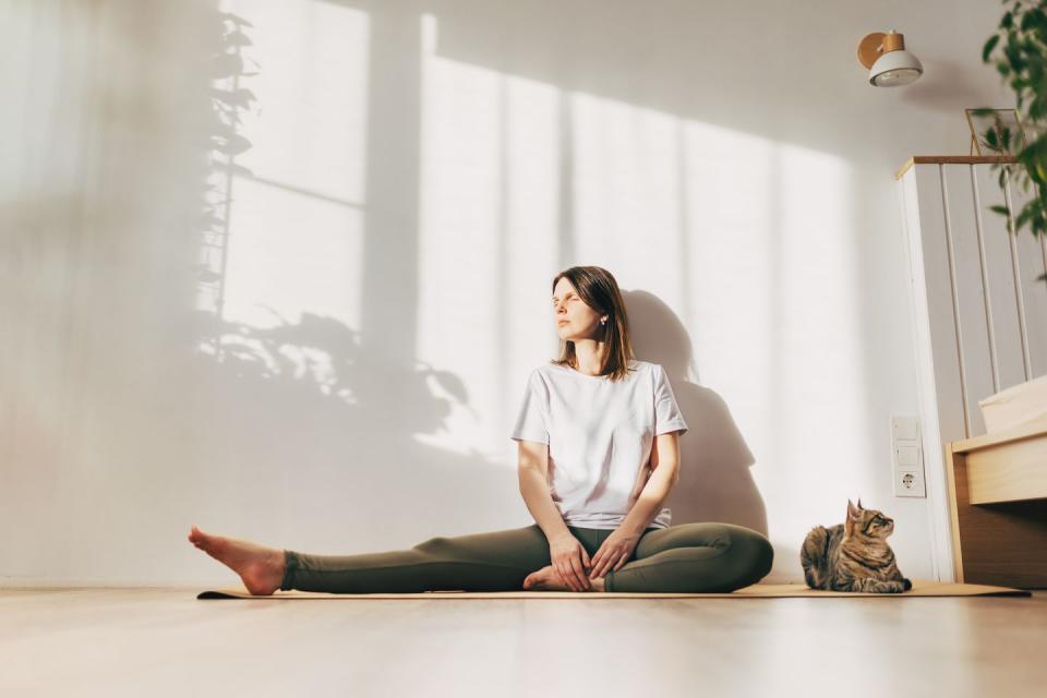 young smiling woman stretching her leg while sat at home on a yoga mat