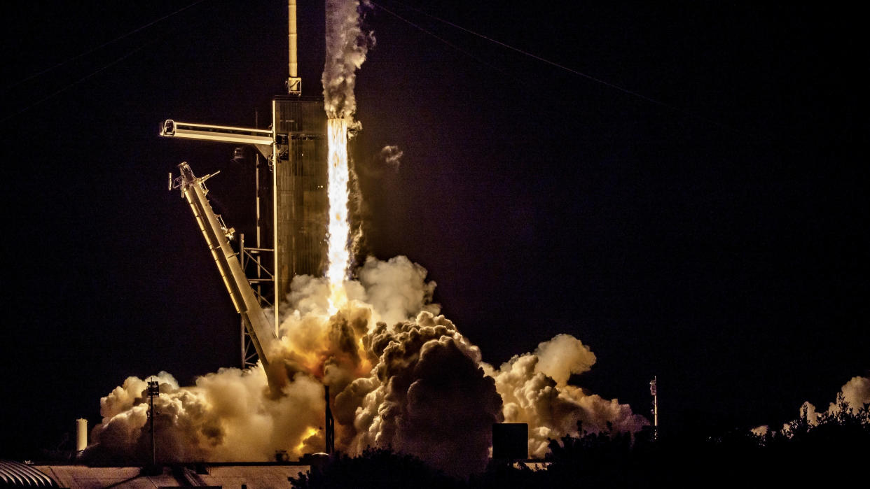  In the dark of night, a rocket blasts fire from its engines, sending plumes of smoke jetting out as it climbs the launch tower out of frame. 