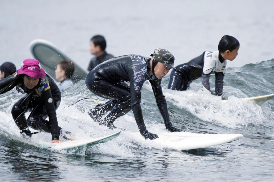 Seiichi Sano, center, an 89-year-old Japanese man, rides a wave with young surfers at Katase Nishihama Beach, Thursday, March 30, 2023, in Fujisawa, south of Tokyo. Sano, who turns 90 later this year, has been recognized by the Guinness World Records as the oldest male to surf. (AP Photo/Eugene Hoshiko)