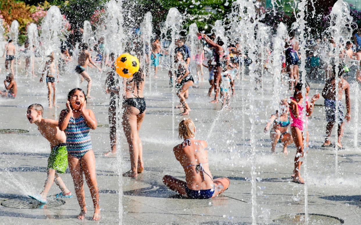 People cool off in water fountains in Paris during this summer's heatwave - AFP