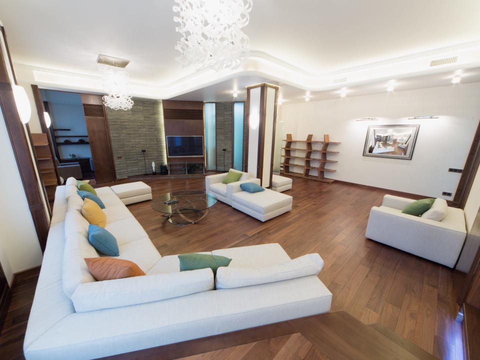 Living room with wooden floor, white couch and chairs, a chandelier and several lights along wall