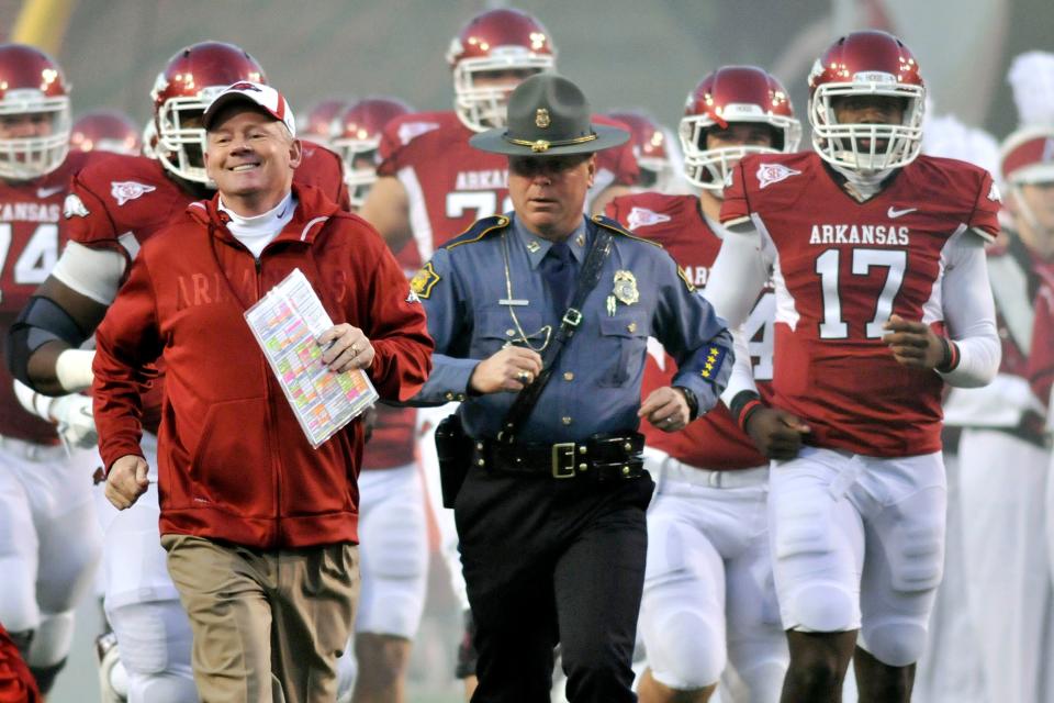 FILE - In this Nov. 12, 2011, file photo, Arkansas coach Bobby Petrino, left, followed by Arkansas State Police Captain Lance King, center, Brandon Mitchell (17) and  and the rest of the team onto the field before the start of an NCAA college football game against Tennessee in Fayetteville, Ark. The Arkansas State Police are taking another look at the motorcycle crash involving coach Petrino. Authorities say they want to know how State Police Captain Lance King wound up meeting Petrino after the crash at an intersection in Fayetteville. King, who provides security for the coach during the season, then drove Petrino to a hospital. (AP Photo/April L. Brown, File)