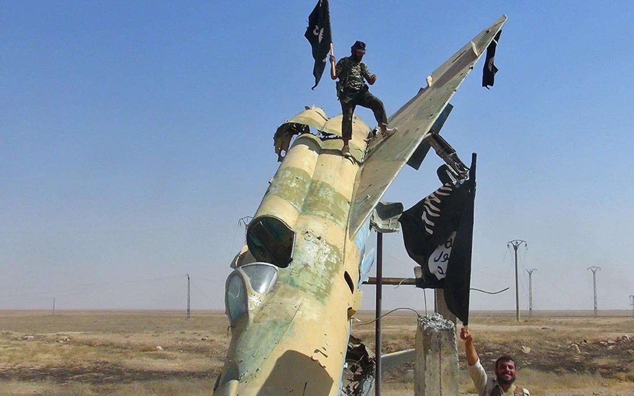 Isil fighters wave the group's flag from a damaged display of a government fighter jet after taking Tabqa air base in 2014 - AP