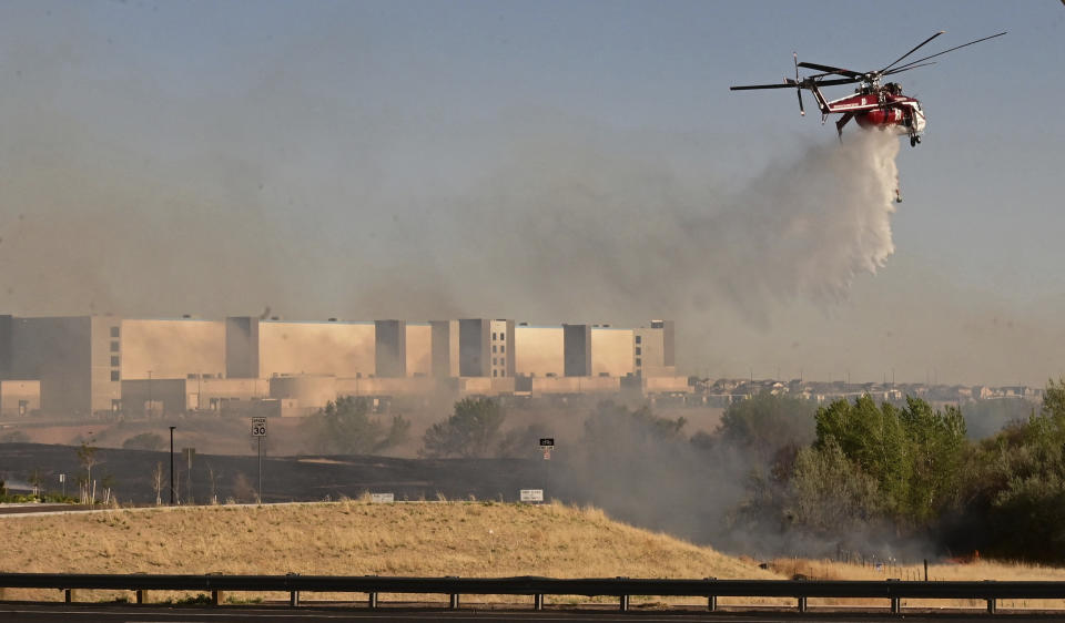 FILE - A helicopter drops water on flames from the Alturas Fire across Powers Blvd. from the Amazon Distribution Center on Thursday, May 12, 2022. A bill introduced in the Colorado legislature would create a $2 million pilot program to use cameras, likely with AI technology, in high-risk locations to help identify fires before they burn out of control. (Jerilee Bennett/The Gazette via AP, File)