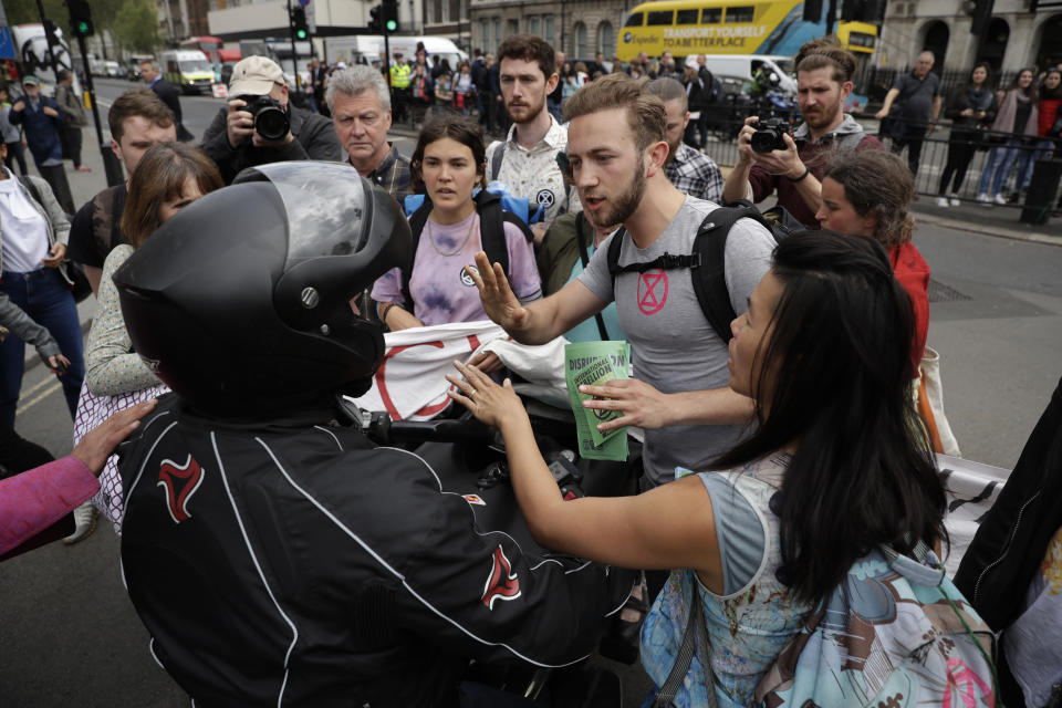 Extinction Rebellion climate change protesters stop a motorcyclist from driving through them as they briefly block the road by Parliament Square in London, Wednesday, April 24, 2019. The non-violent protest group, Extinction Rebellion, is seeking negotiations with the government on its demand to make slowing climate change a top priority. (AP Photo/Matt Dunham)