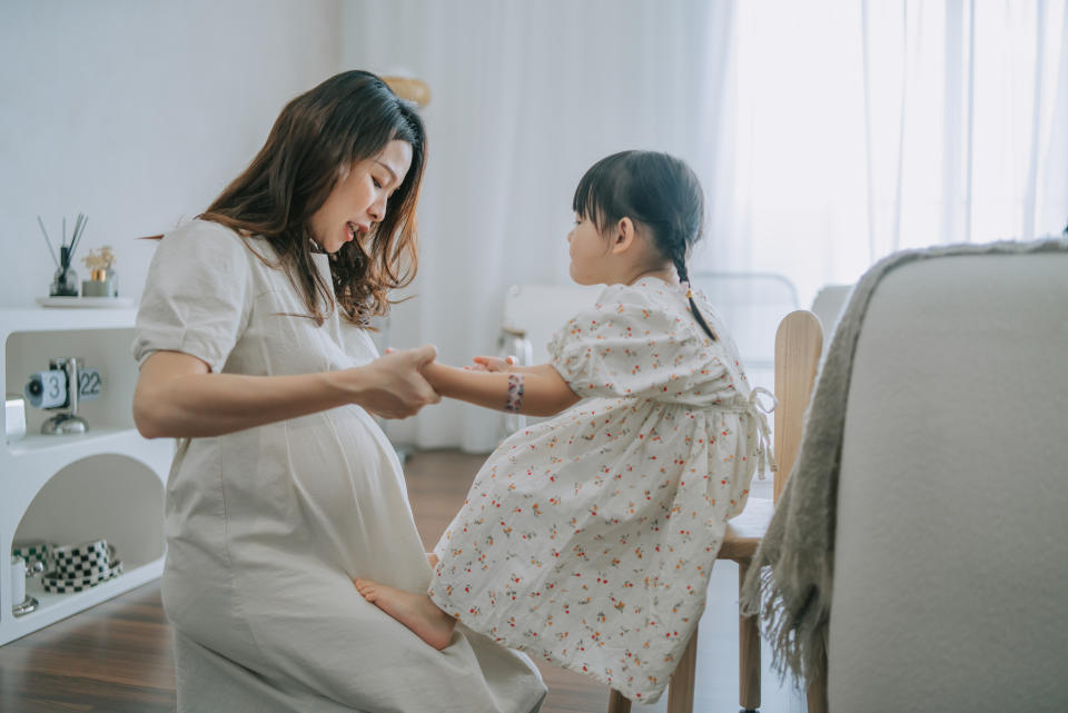 happy Chinese Mother holding daughter hands talking to her in living room