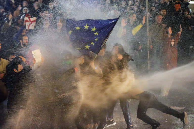 Manifestantes sostienen una bandera de la Unión Europea son rociados por un cañón de agua durante los enfrentamientos con la policía antidisturbios cerca del parlamento georgiano en Tiflis el 7 de marzo de 2023.