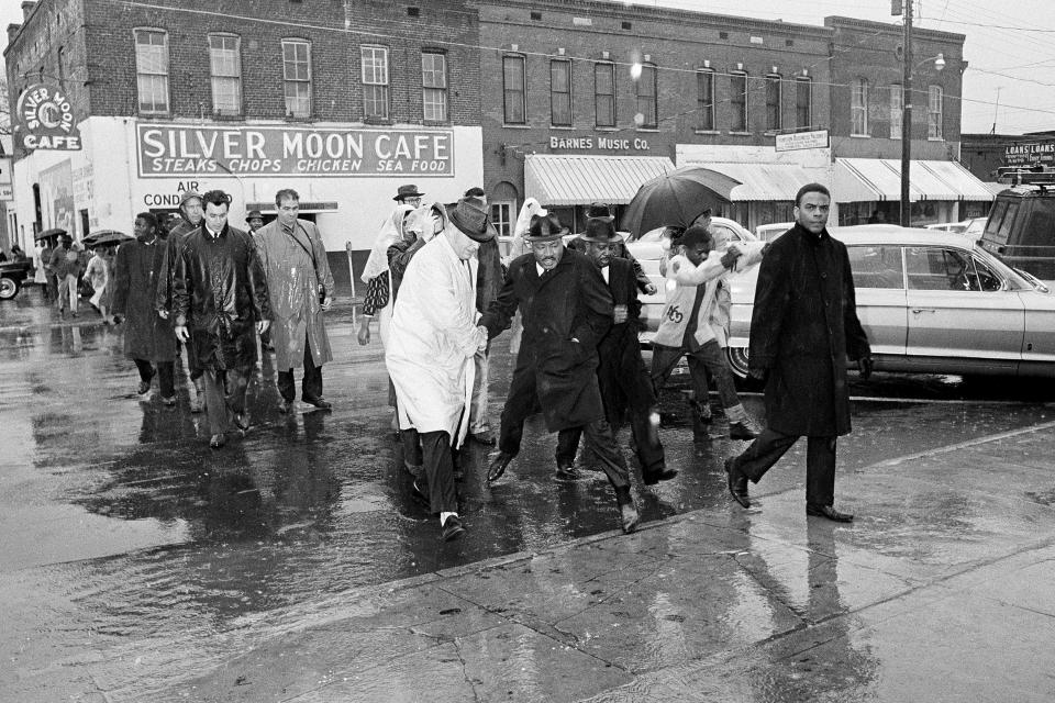FILE - With civil rights activist Andrew Young at right, the Rev. Martin Luther King Jr. hops over a puddle as it rains in Selma, Ala., on March 1, 1965. King led hundreds of African Americans to the court house in a voter registration drive. At right, behind King is Rev. Ralph Abernathy. (AP Photo/File)